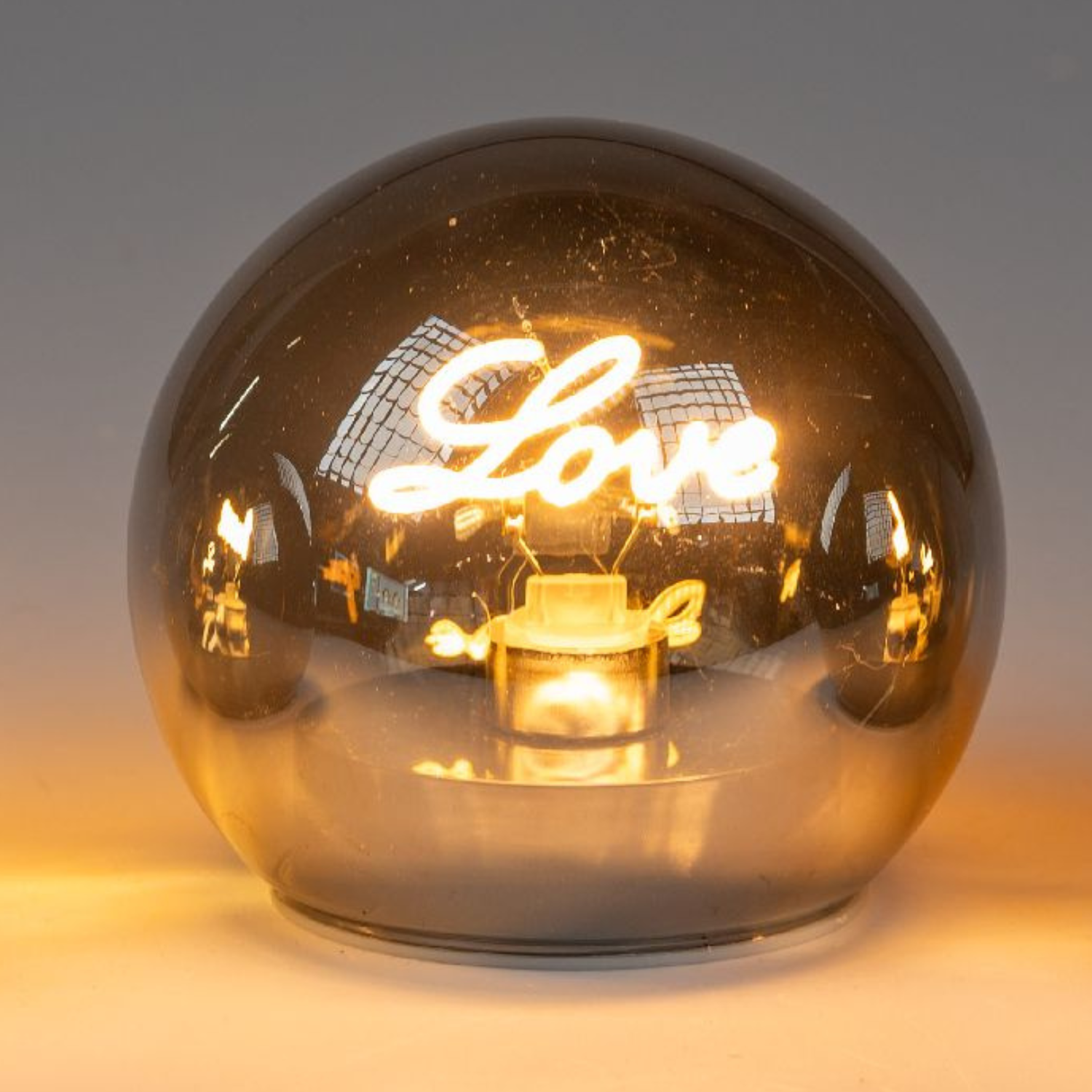 Drei gläserne Lampen mit einem warmen Licht, die das Wort ""Love"" in einer geschwungenen Schrift ze