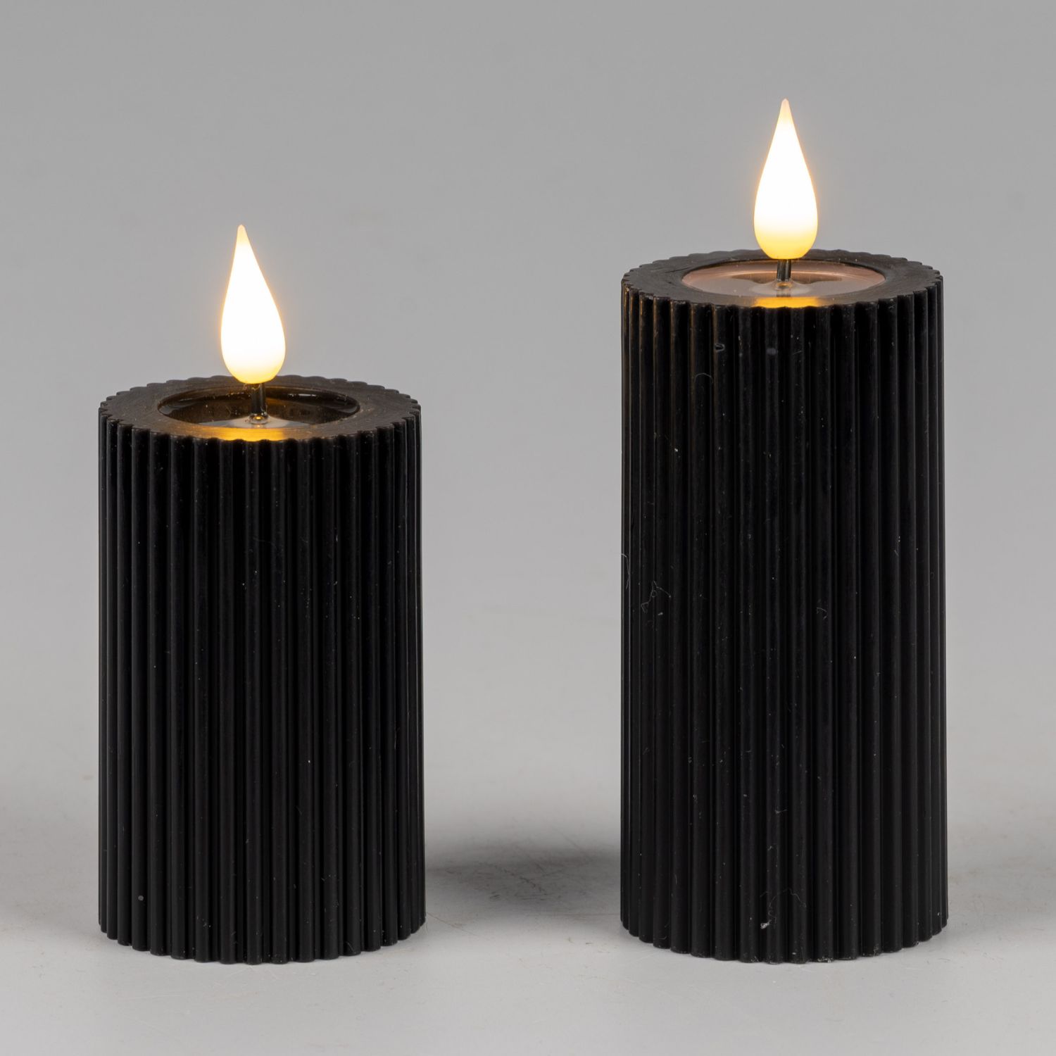 Zwei schwarze geriffelte Kerzen in unterschiedlicher Höhe mit brennender Flamme