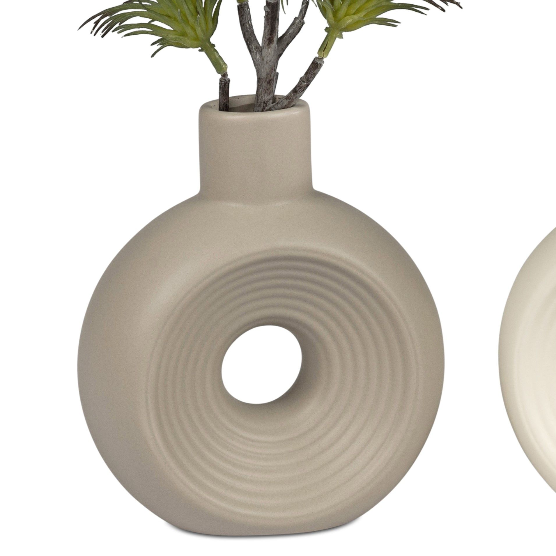 Eine runde, beige Vase mit einem zentralen Loch und wellenförmigen Mustern, in der grüne Zweige stecken.