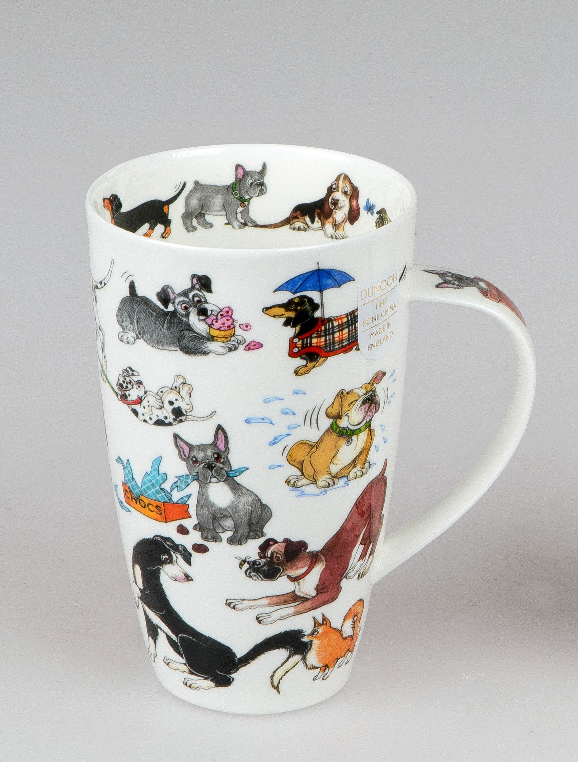 Tasse mit bunten Hundemotiven, darunter verschiedene Hunderassen und spielende Hunde, auf weißem Hintergrund.