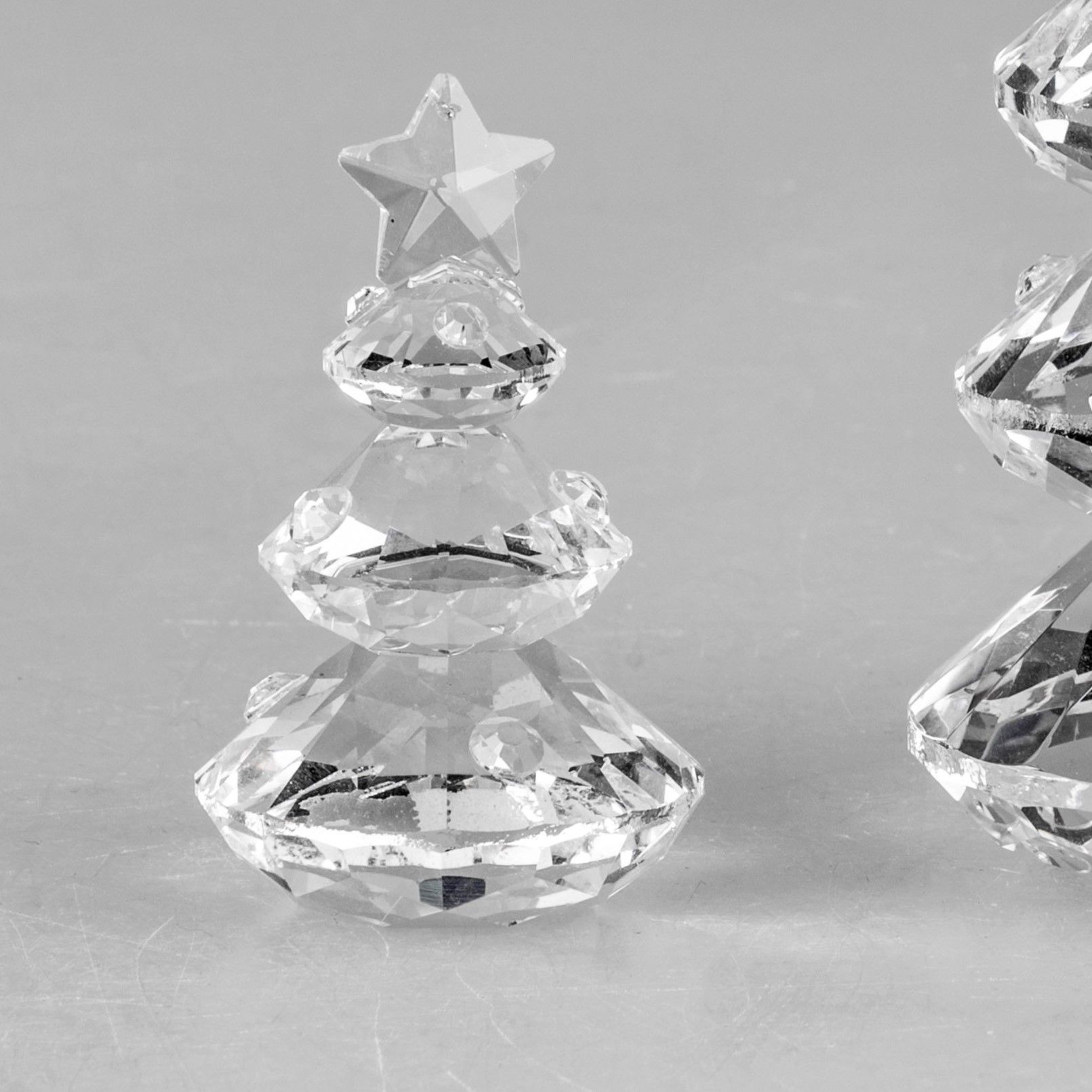 Zwei gläserne Weihnachtsbaumfiguren mit Sternen an der Spitze, auf einer grauen Oberfläche platziert