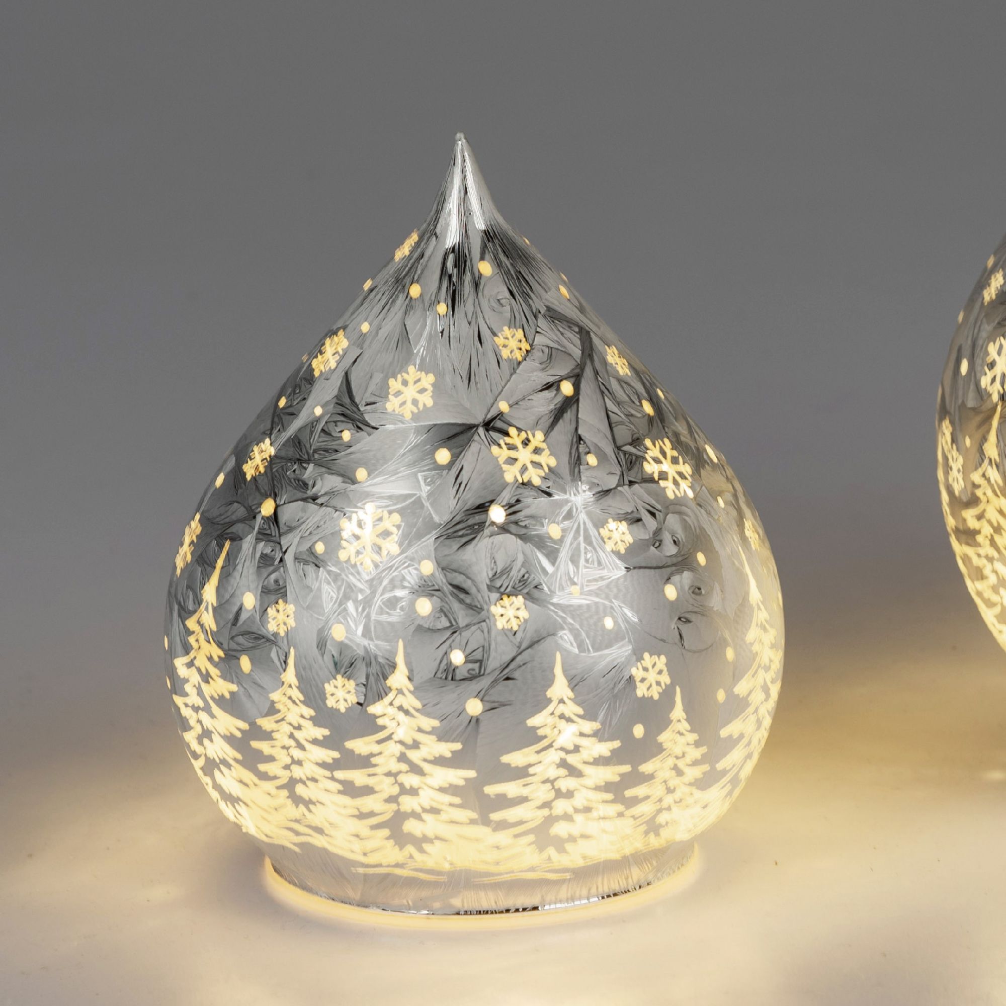 Dekorative, gläserne Weihnachtskugel in Tropfenform mit weißen Schneeflocken und Tannenbäumen, sanft