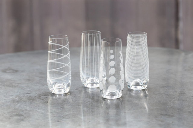 Vier verschiedene Gläser aus klarem Glas stehen auf einer Tischoberfläche. Jedes Glas hat ein einzigartiges Muster.