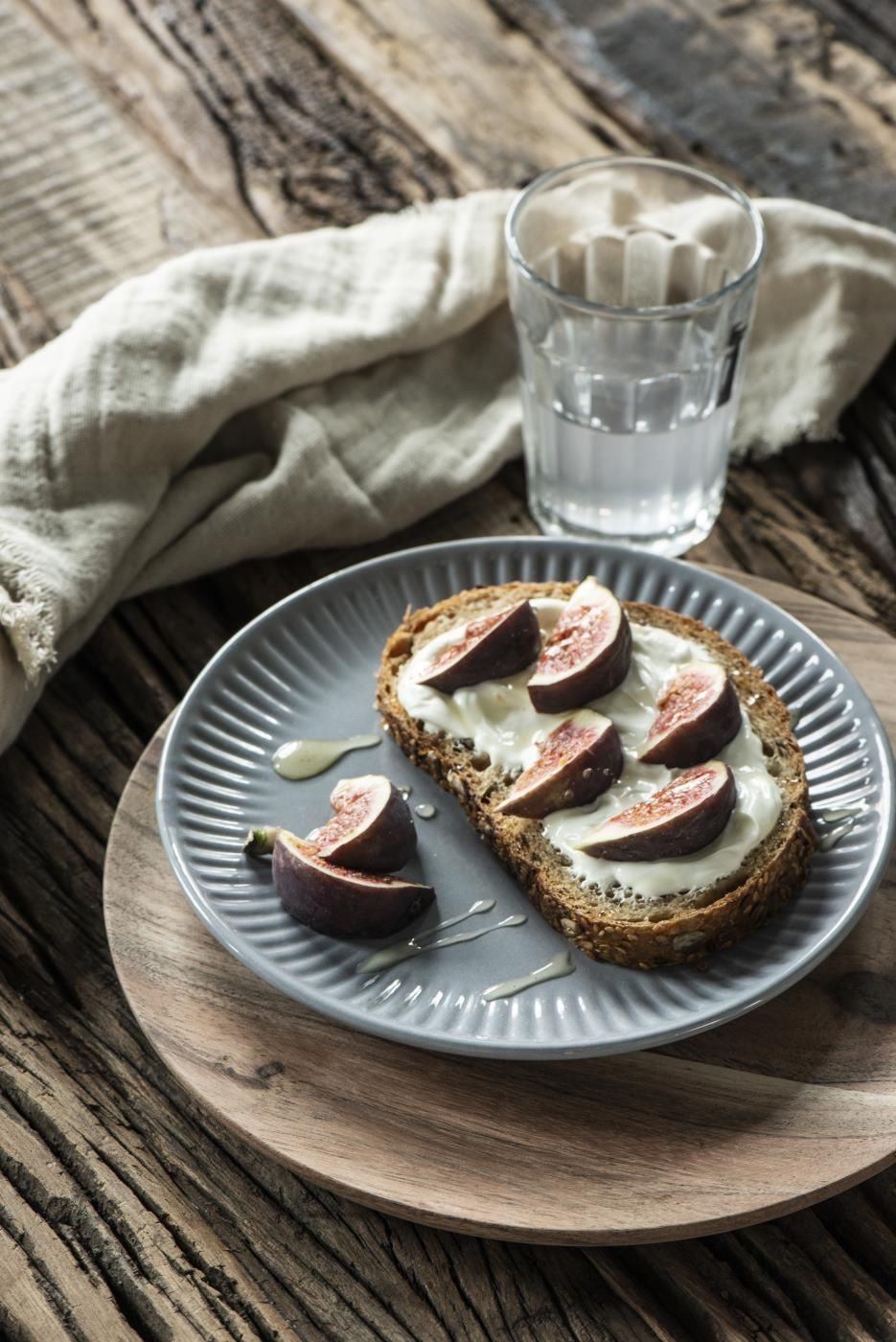 Ein Teller mit einem belegten Brot, belegt mit Frischkäse und Feigen, daneben ein Glas Wasser auf einem Holztisch.