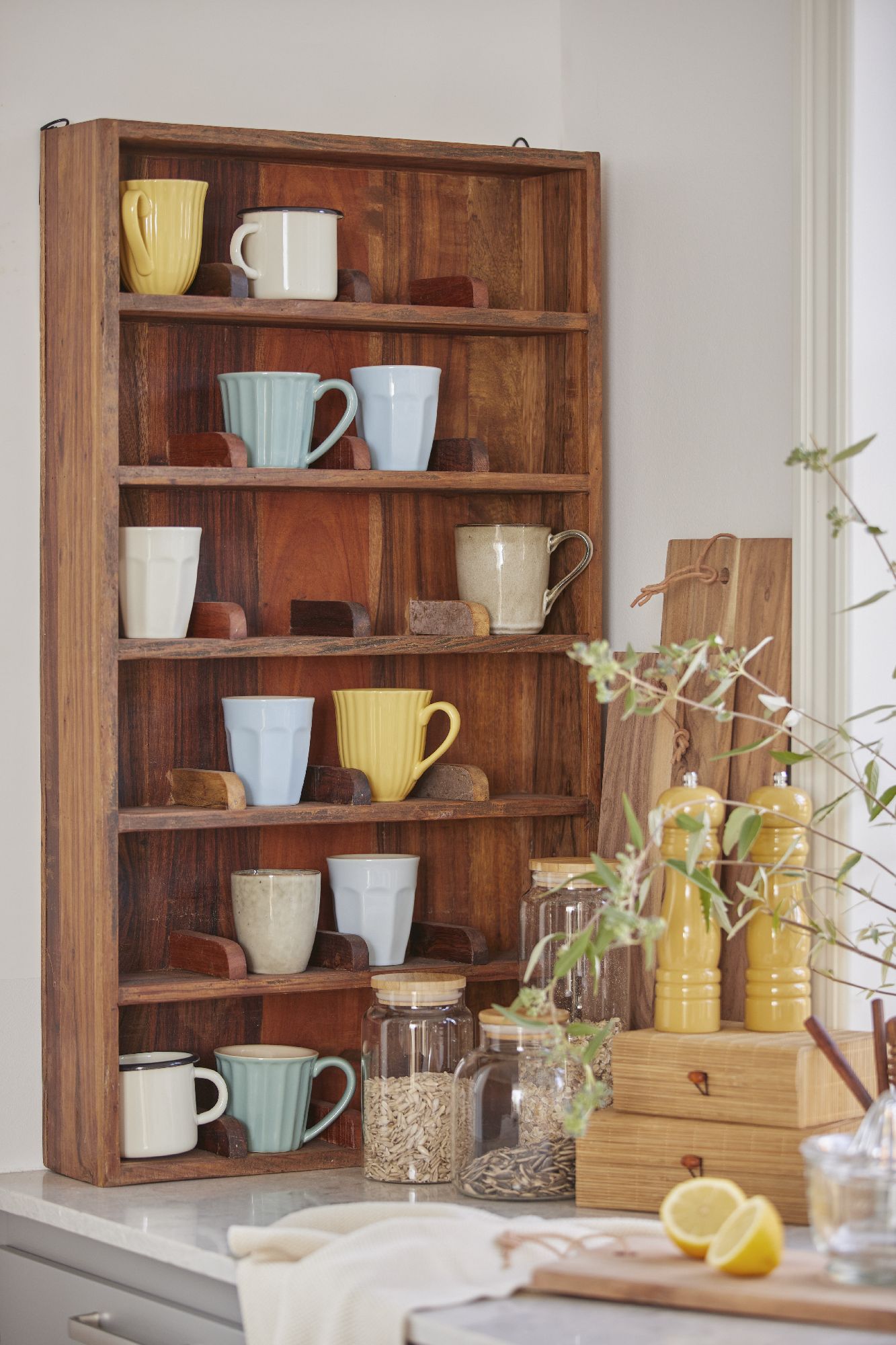 Regal aus Holz mit mehreren Regalböden, darauf stehen verschiedene Tassen in unterschiedlichen Farben und Formen sowie Gläser und Gewürzmühlen.