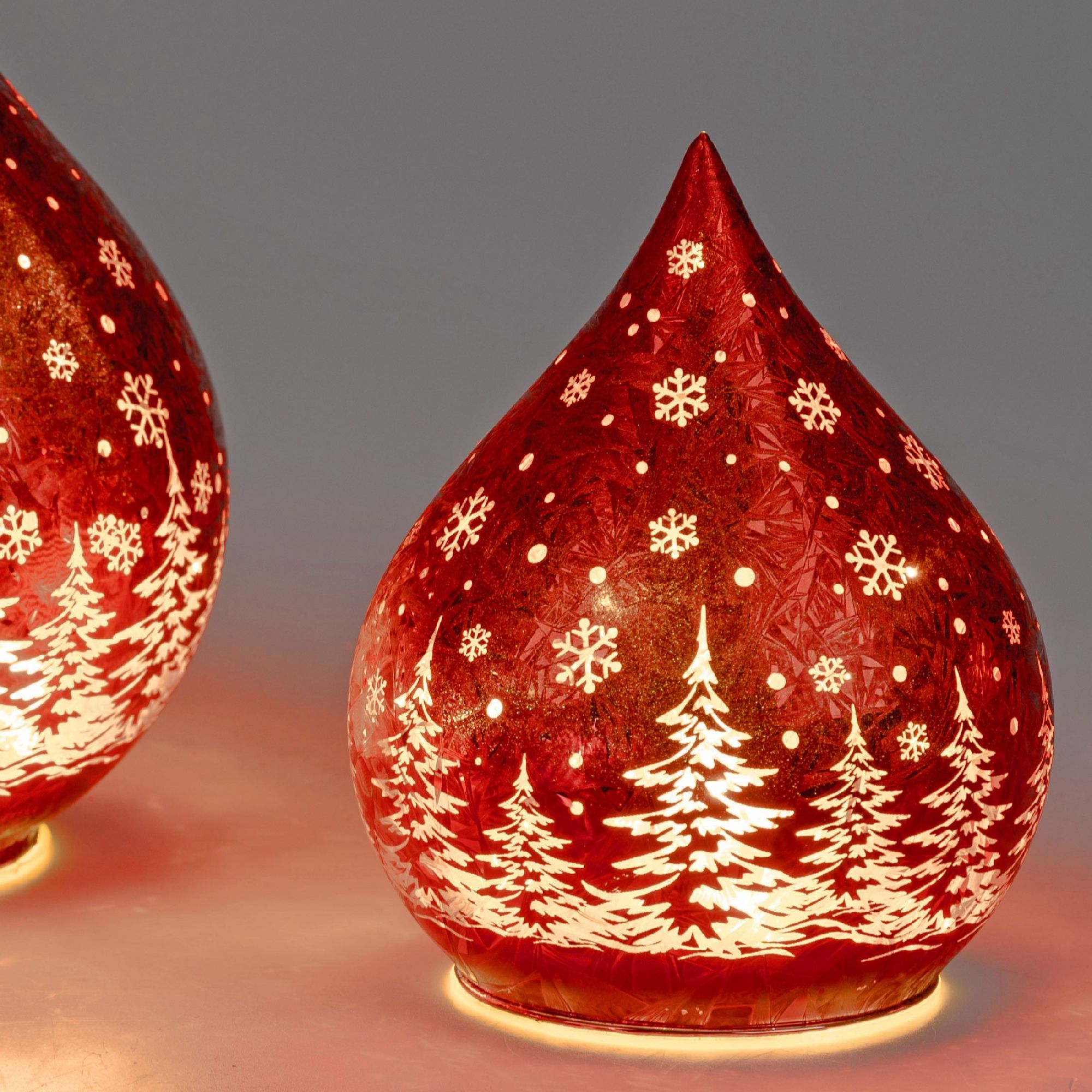 Zwei rote, tropfenförmige Weihnachtslichter mit weißen Schneeflocken und Tannenbaum-Motiven auf der