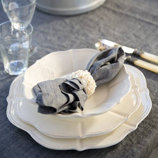 Ein gedeckter Tisch mit mehreren Tellern, einem Stoffserviettenring und Gläsern auf einem grauen Tischcloth.