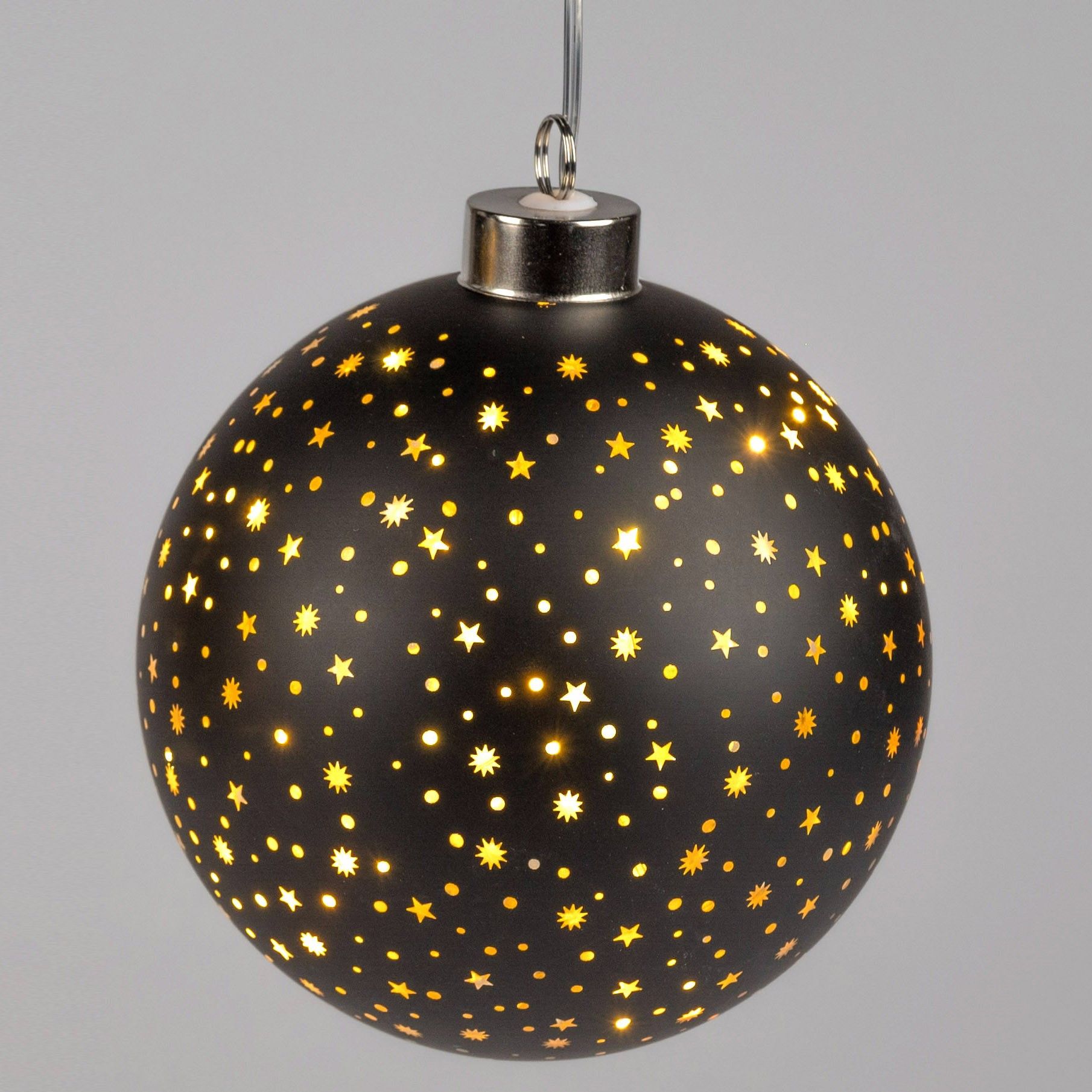 Schwarze Weihnachtskugel mit goldenen Sternen und kleinen Löchern, durch die Licht strahlt, hängt an