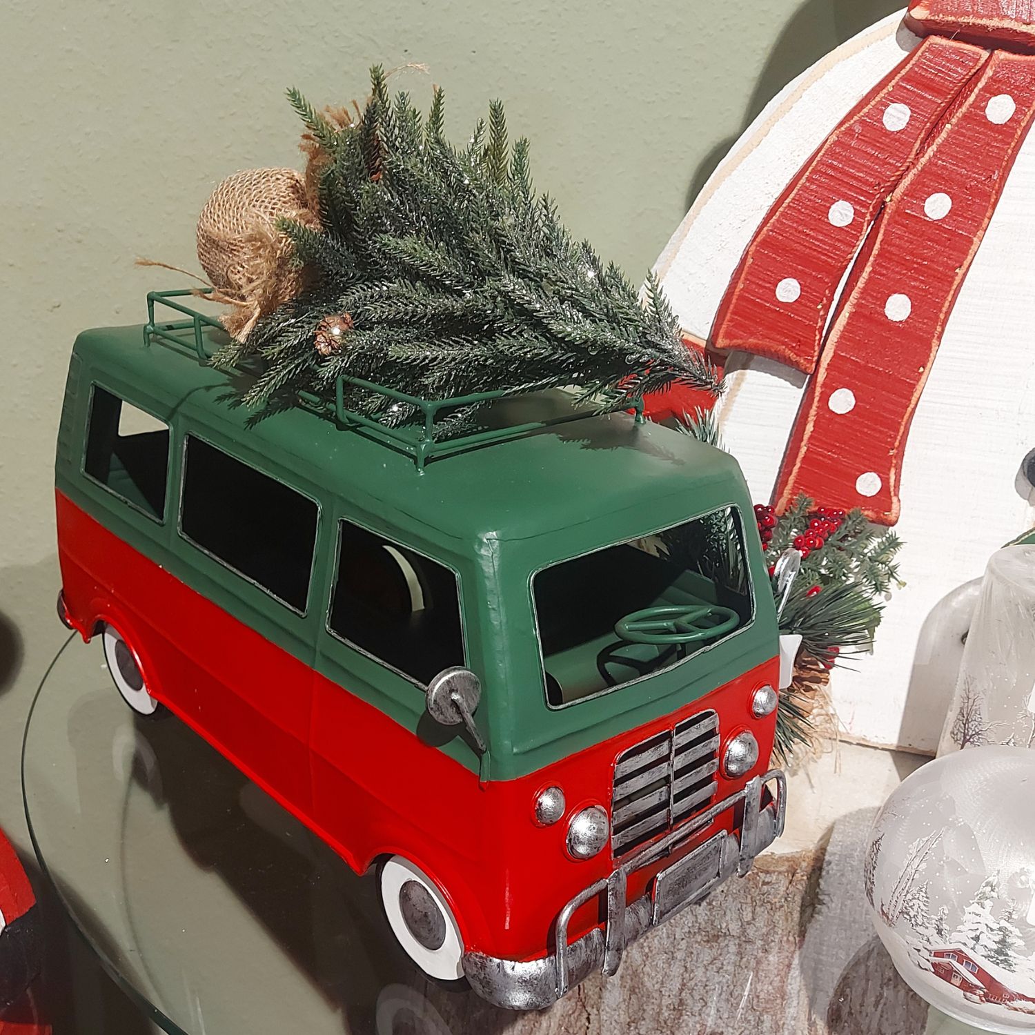 Miniaturbus in Grün-Rot mit Tannenbaum auf dem Dach, weihnachtliche Deko im Hintergrund