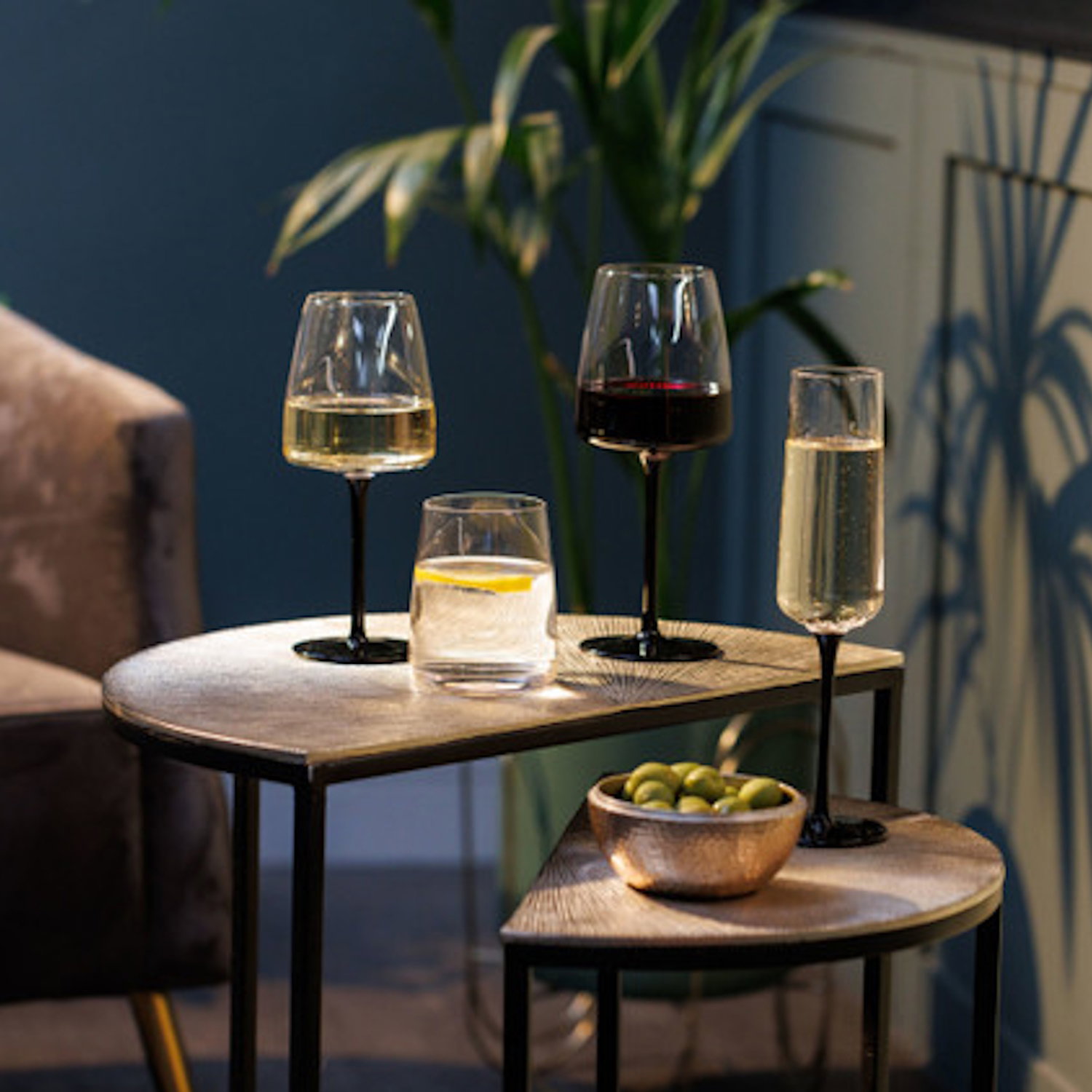 Auf einem Tisch stehen vier Gläser: zwei Weingläser, ein Glas mit Zitrone und ein Sektglas. Daneben eine Schale mit Oliven.