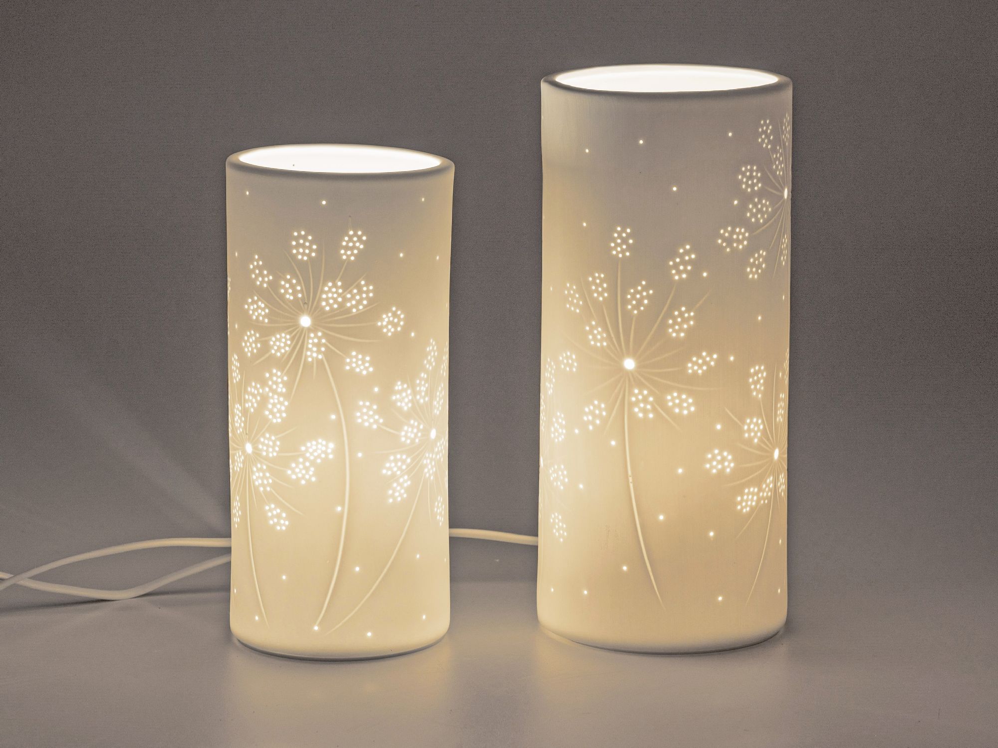Zwei dekorative Lampen in zylindrischer Form mit floralem Muster, die sanftes Licht ausstrahlen.