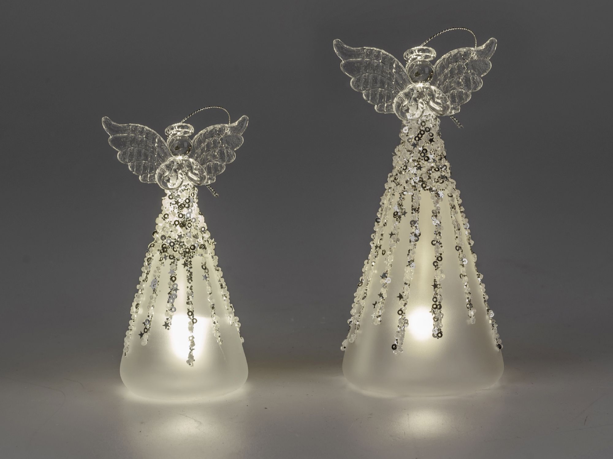 Zwei dekorative Engel aus Glas mit transparenten Flügeln und glitzernden Details, die sanft beleucht