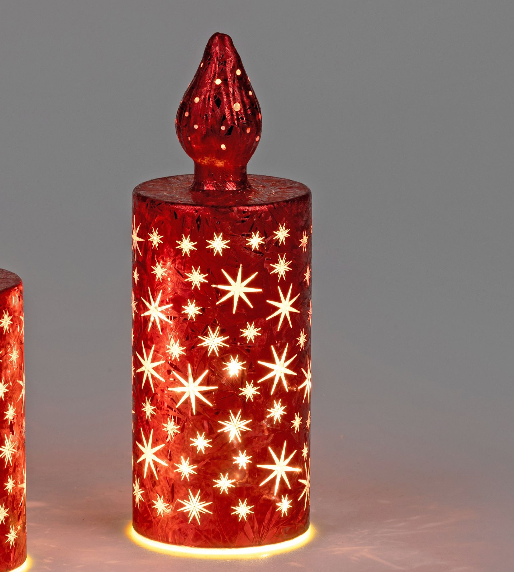 Rote Kerze mit sternförmigen Mustern, die von innen beleuchtet ist. Die Kerze hat eine spitze Form o