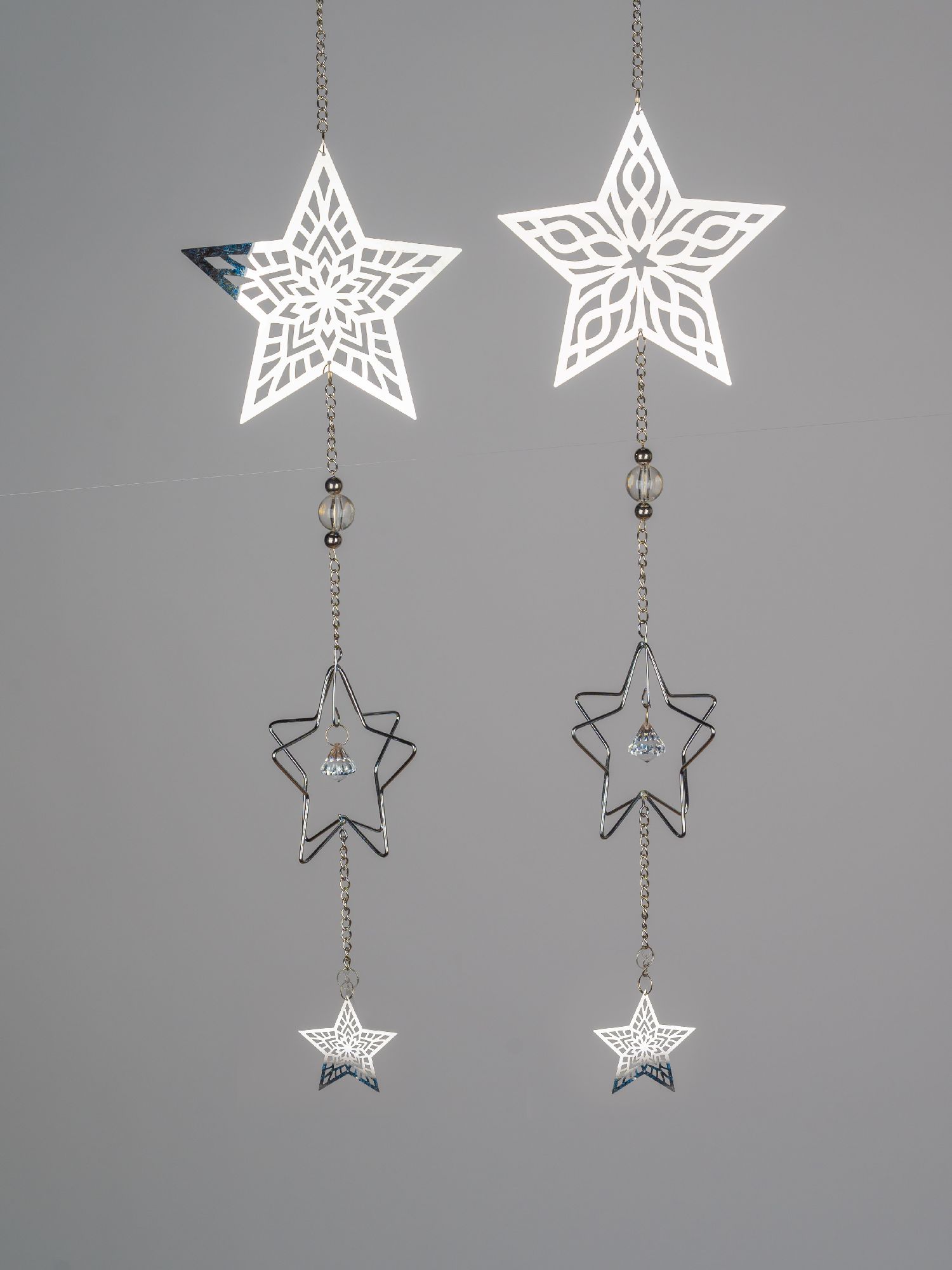 Zwei hängende Sterne aus Metall, einer mit filigranem Muster, der andere schlicht, beide mit kleinen