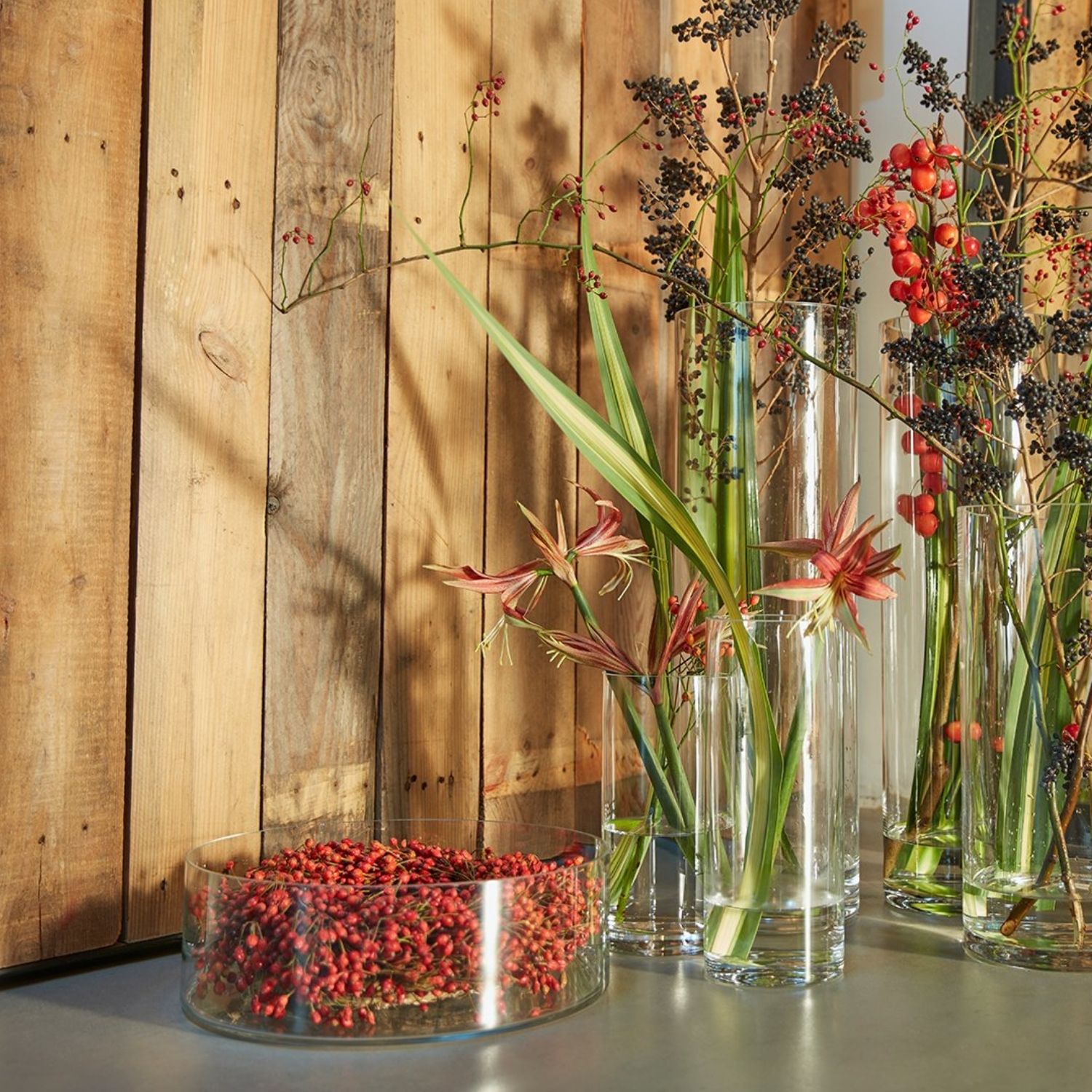 Glaschale und Glasvasen vor Holzwand mit Blumen Dekoriert