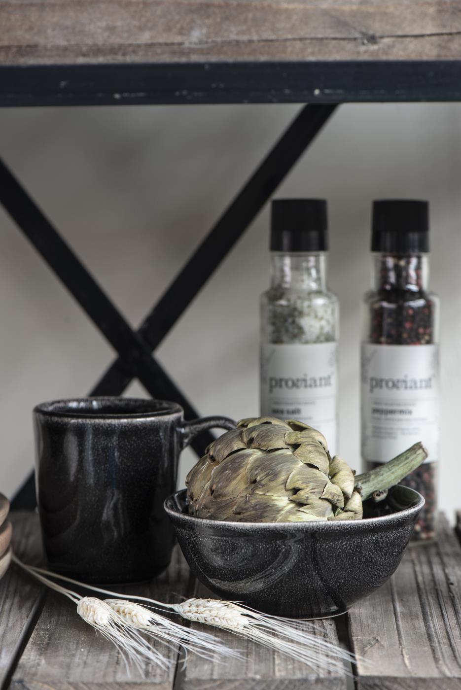 Schwarze Tasse und Schüssel mit Artischocke, daneben Gewürzgläser und Weizenhalme auf einem Holzregal.