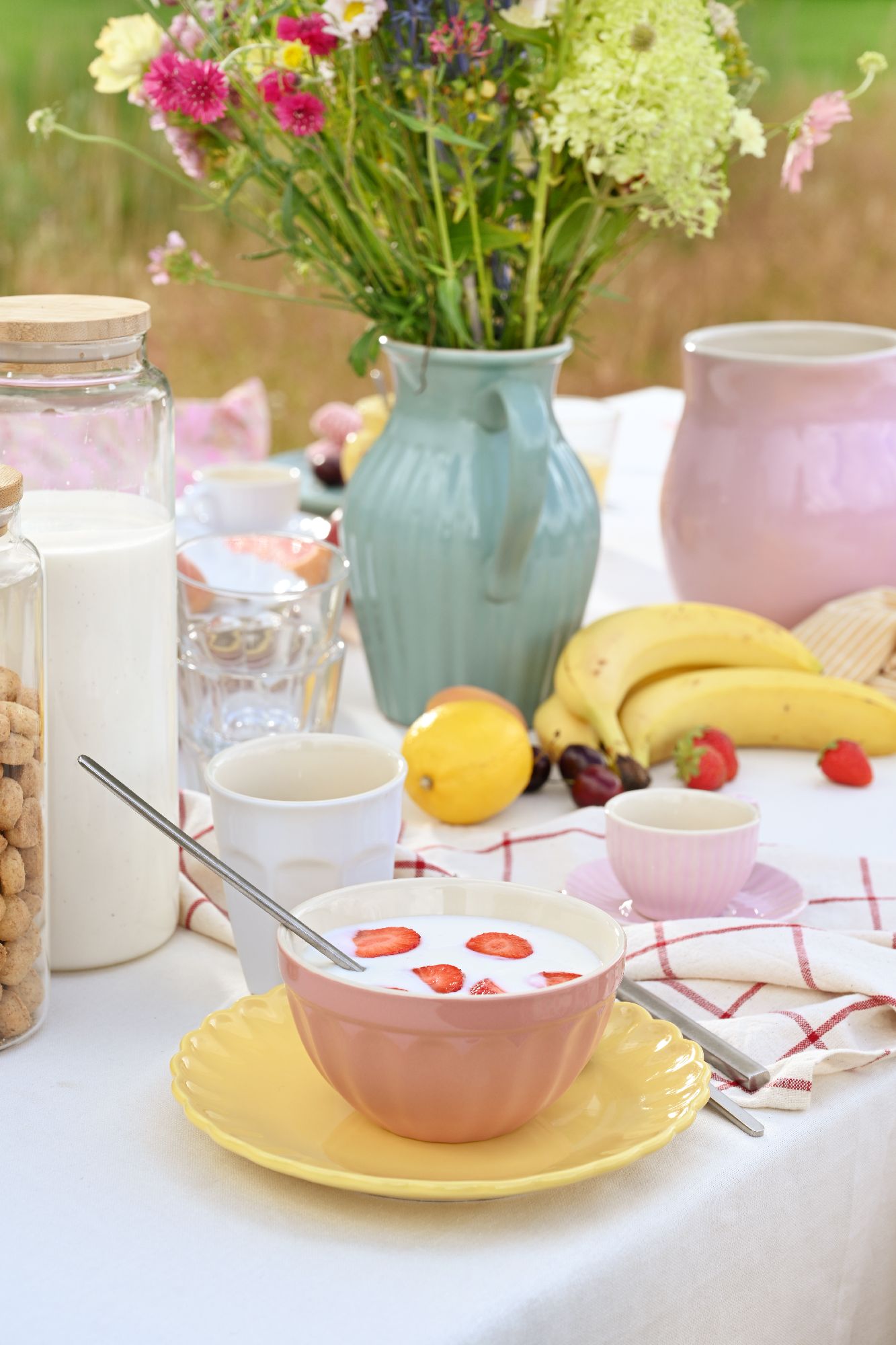Ein gedeckter Tisch mit einer Schüssel Joghurt, frischen Erdbeeren, Obst, Blumen und verschiedenen Getränken.