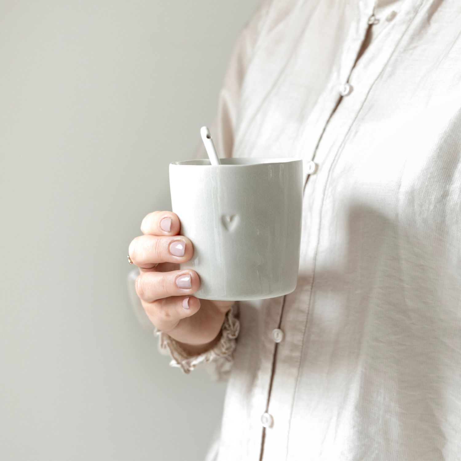 Hand mit heller Tasse und Löffel, kleines Herzrelief, Person in heller Bluse
