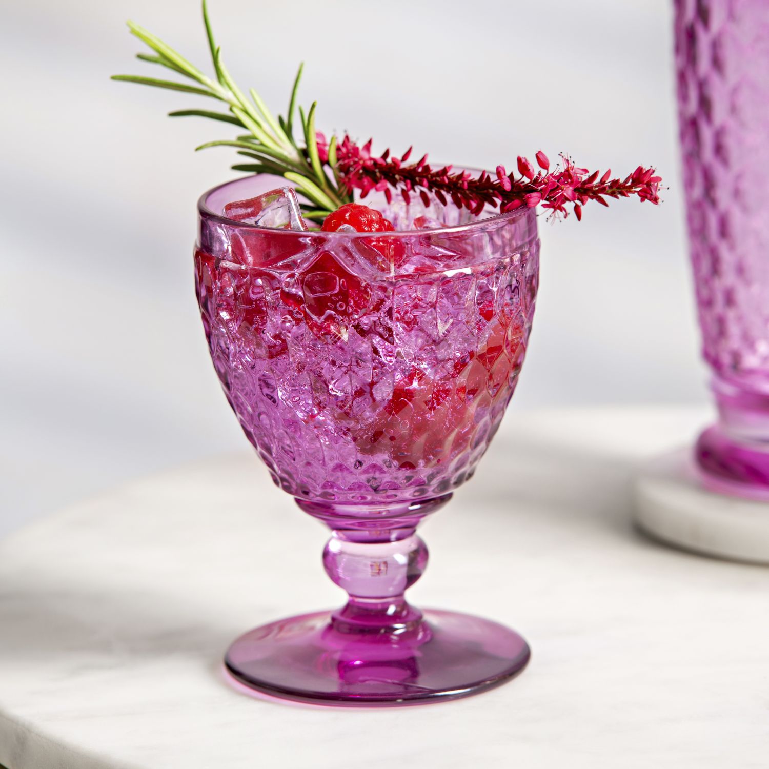 Lila Glas mit Eis und Beeren, dekoriert mit Rosmarin und roten Blüten