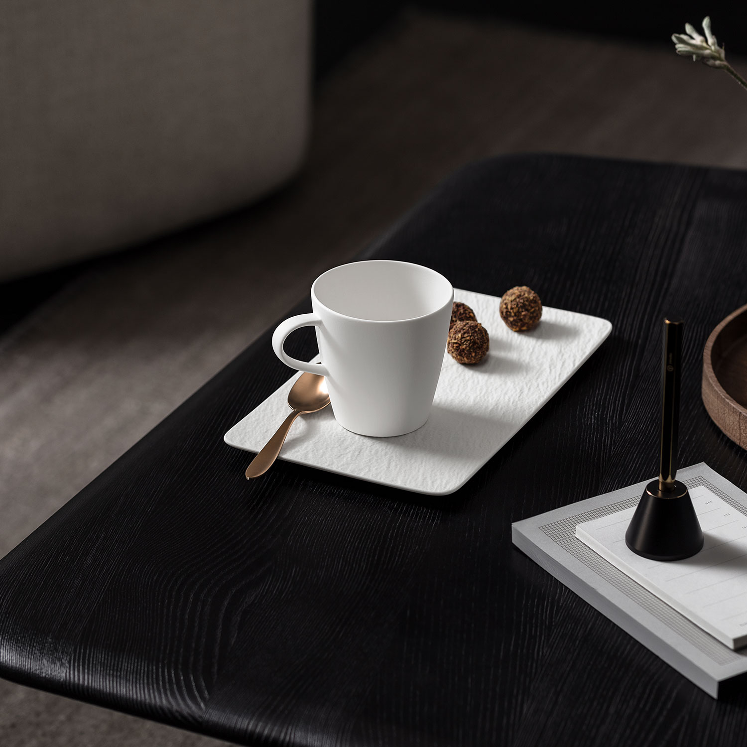 Eine weiße Tasse steht auf einem weißen Untersetzer, daneben liegen drei runde Snacks und ein goldener Löffel.