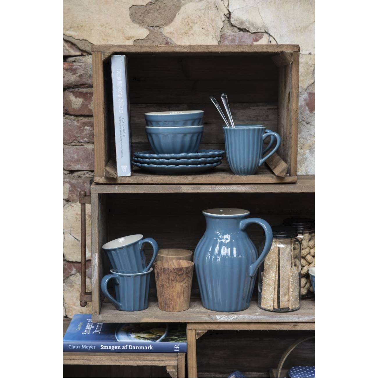 Regal mit blauen Geschirrteilen: Tassen, Schalen, ein Krug und ein Glasbehälter. Im Hintergrund ein Buch und eine Holzschale.