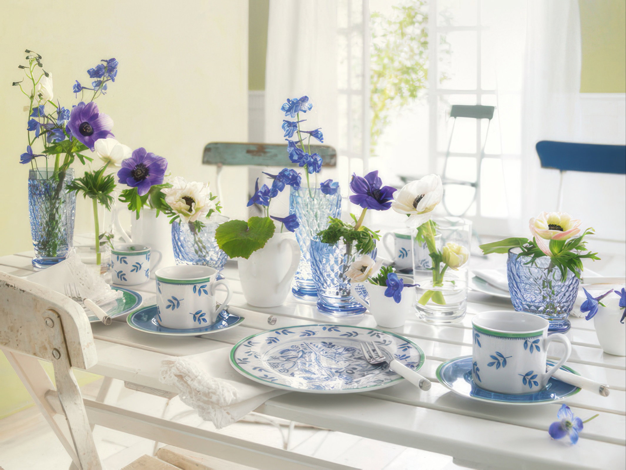 Ein gedeckter Tisch mit blau-weißer Porzellangeschirr und Vasen voller bunter Blumen in einem hellen