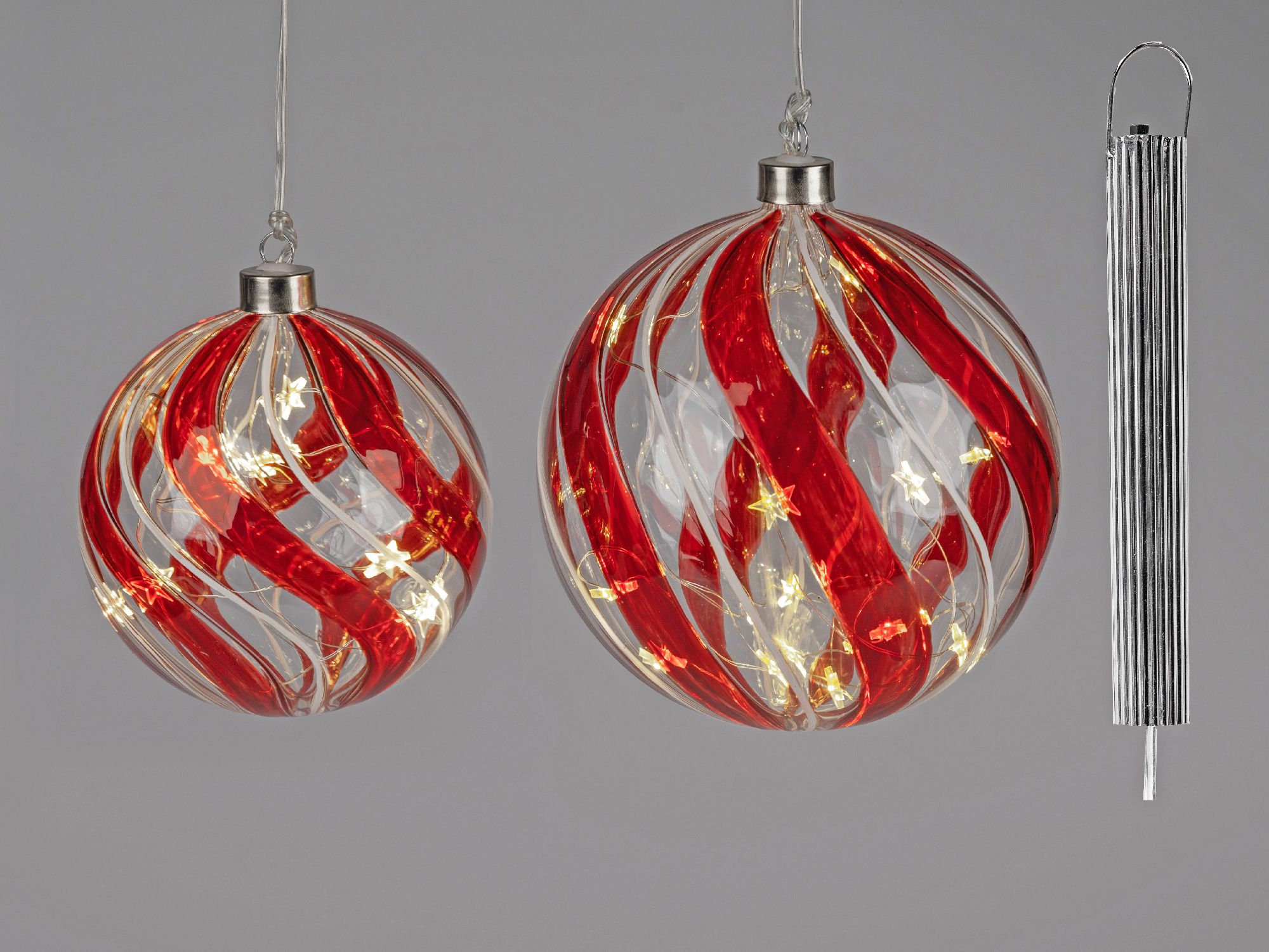 Zwei hängende Weihnachtskugeln in Rot und Transparent mit Lichtern, daneben ein silberner Aufhänger.