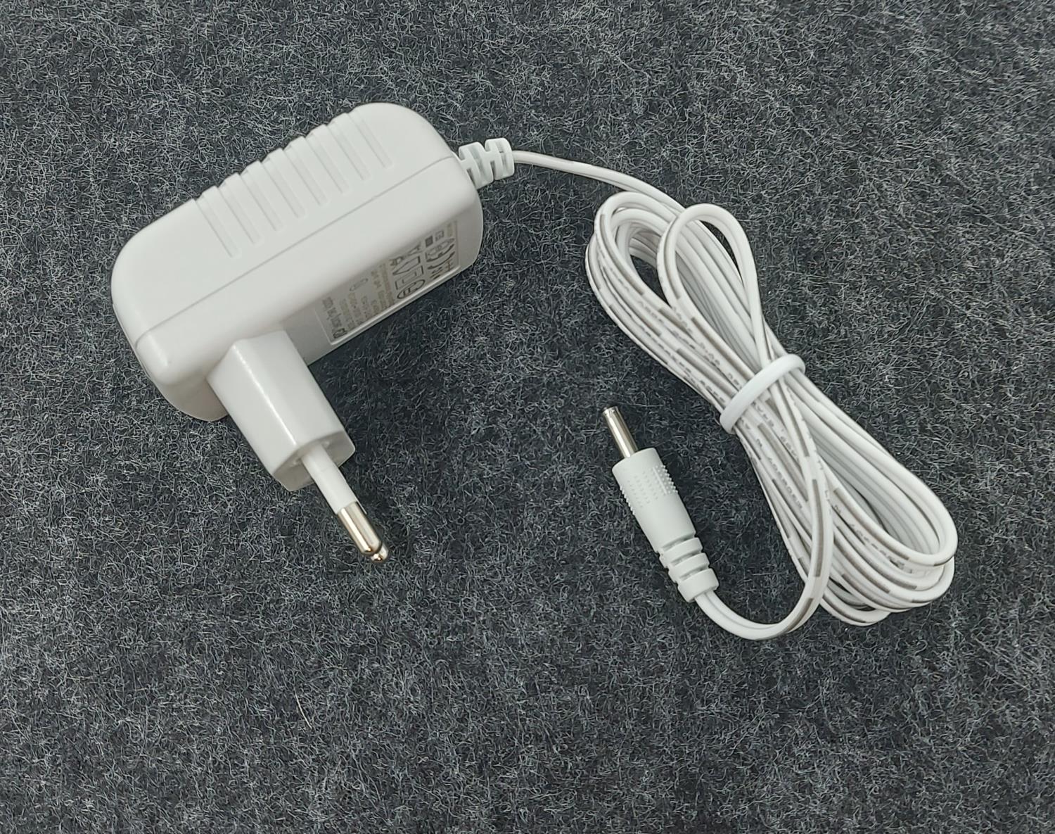 Weißes Netzteil mit Stecker und Kabel, das auf einem grauen Untergrund liegt. Kabel endet in einem r