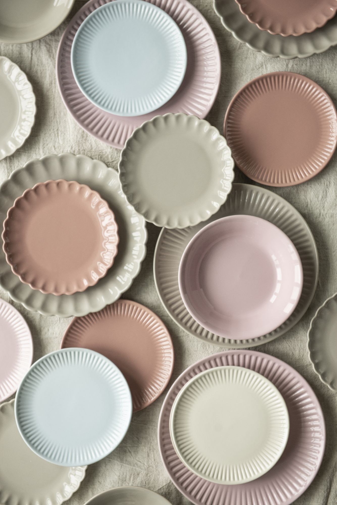 Bunte Teller in verschiedenen Größen und Farben (blau, rosa, beige) liegen übereinander auf einer hellen Oberfläche.