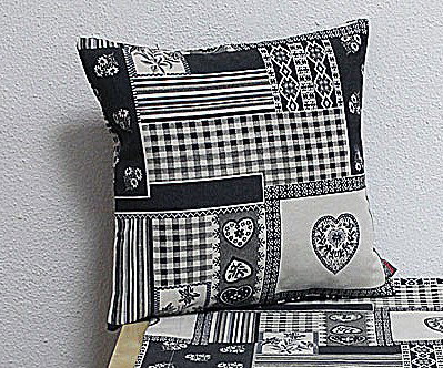 Kissen mit Patchwork-Muster in Schwarz-Weiß, bestehend aus verschiedenen Stoffen und Motiven, auf einem Tisch liegend.