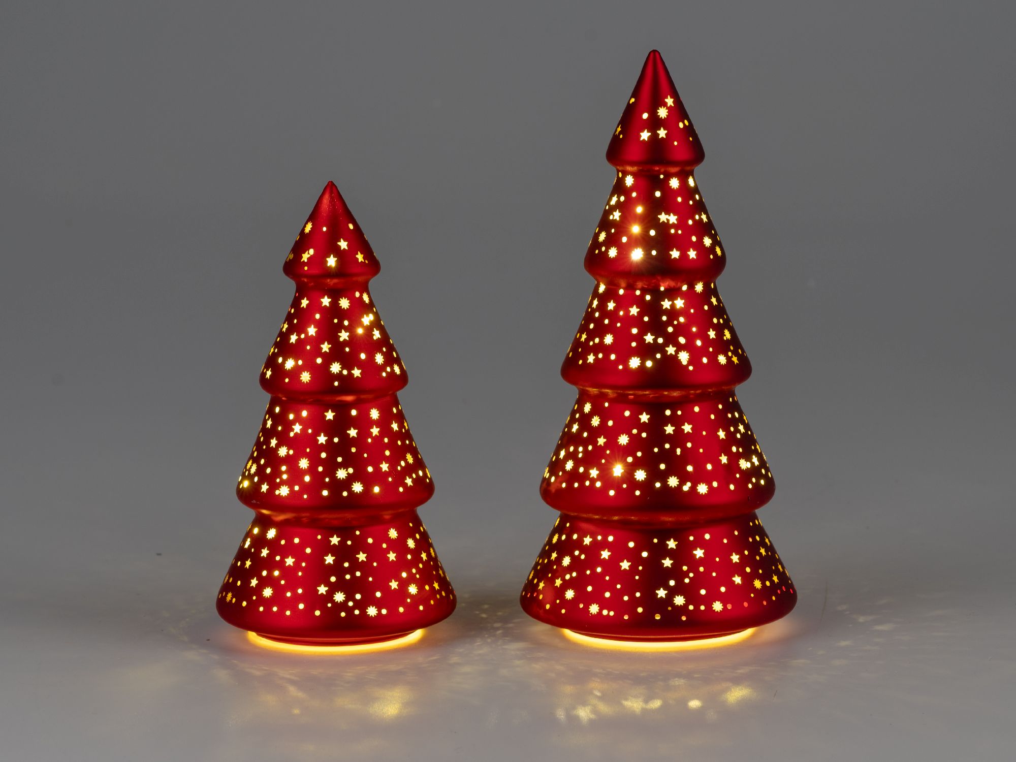 Zwei rote Weihnachtsbaum-Dekorationen mit Sternenmustern, die von innen beleuchtet sind, stehen vor