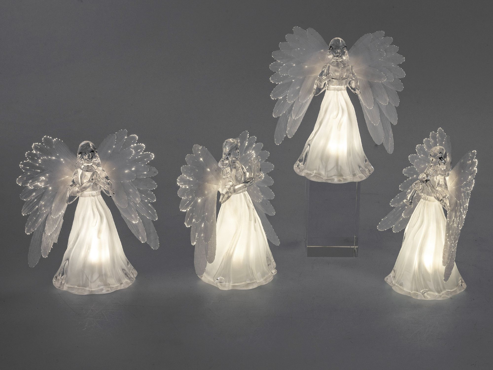 Vier Engel-Figuren aus transparentem Material mit leuchtenden Elementen, stehen auf einem grauen Hin