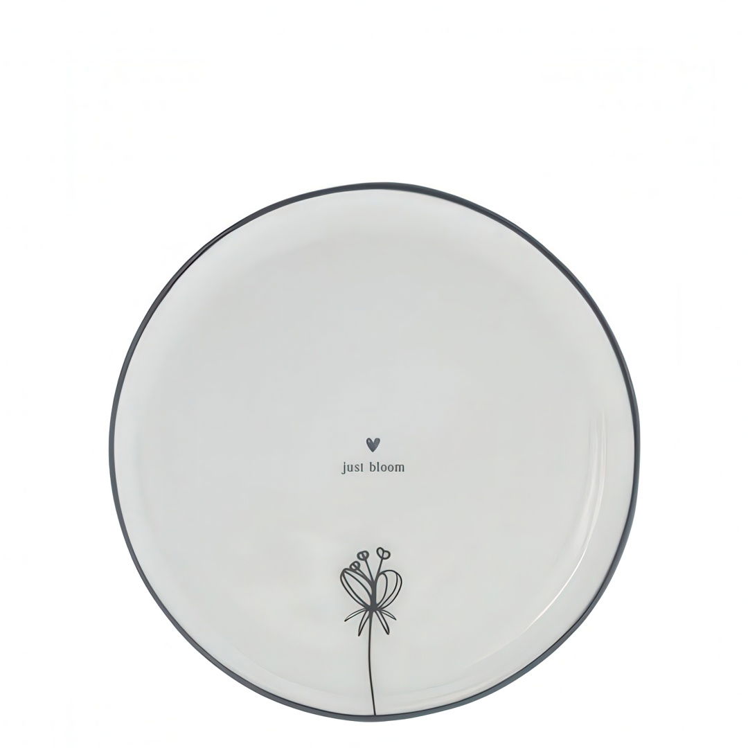 Runder Teller mit schwarzem Rand, bedruckt mit einer Blume und dem Text „just bloom“ in der Mitte.