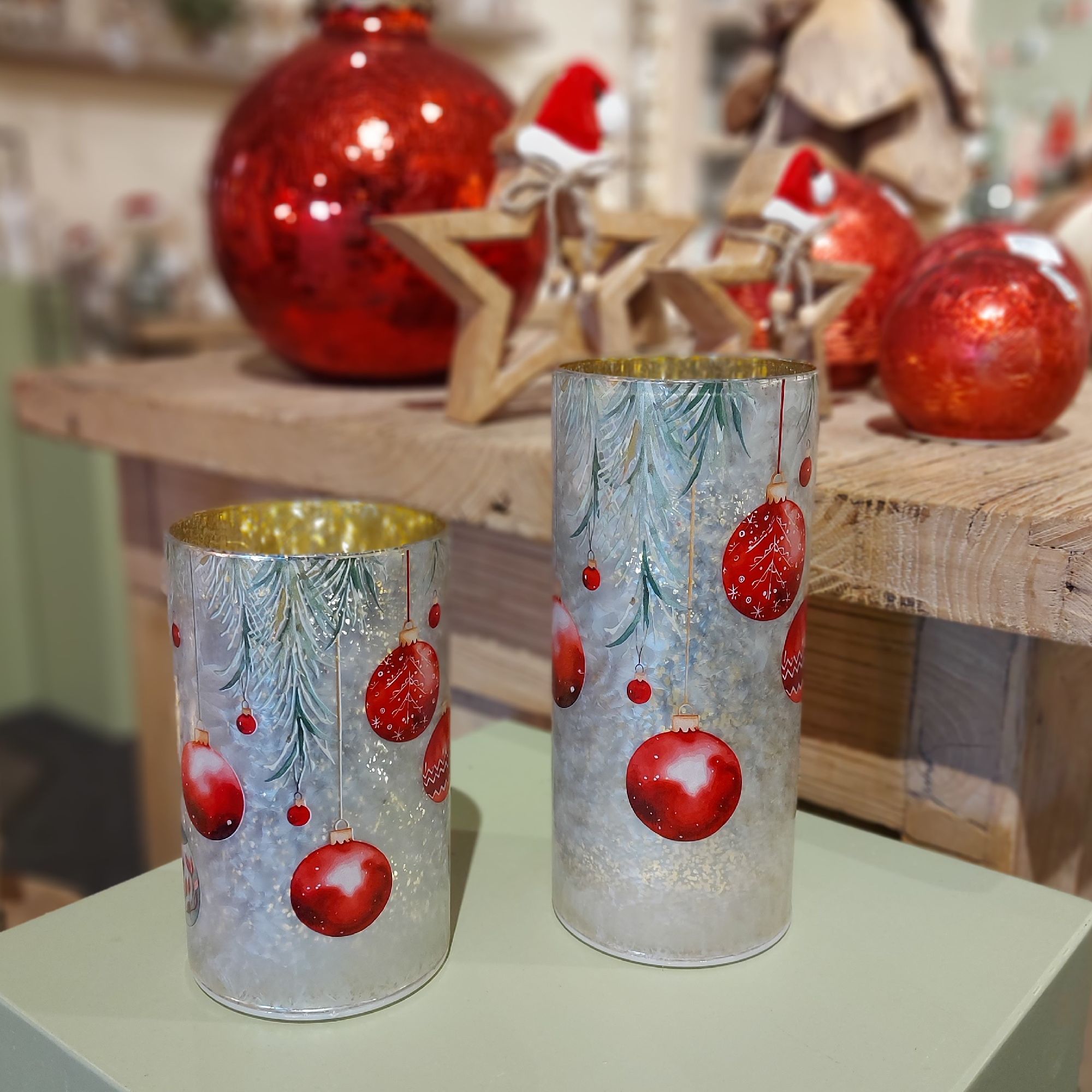 Zwei dekorative Kerzenhalter mit roten Weihnachtskugeln und Tannenzweigen, auf einem Holztisch mit w