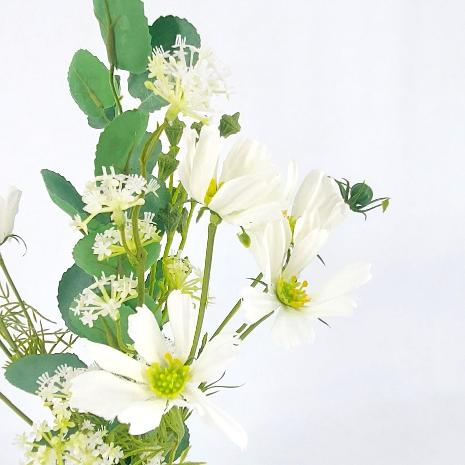 Ein Arrangement aus weißen Blumen und grünen Blättern vor einem hellen Hintergrund.