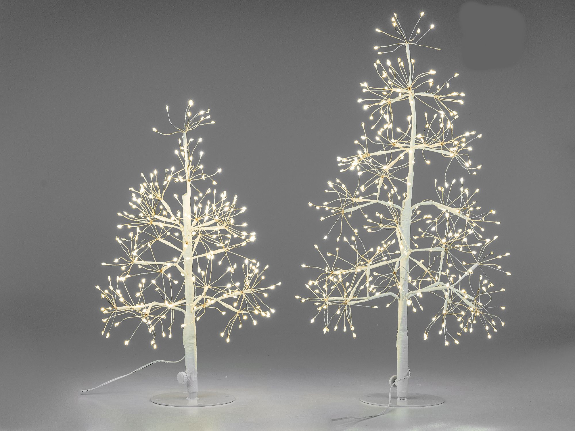 Zwei dekorative, beleuchtete Weihnachtsbäume auf grauem Hintergrund