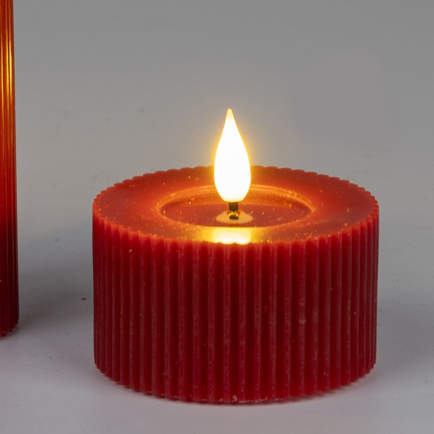 Rote Kerze mit flackerndem Licht auf grauem Hintergrund. Die Kerze hat eine geriffelte Oberfläche un