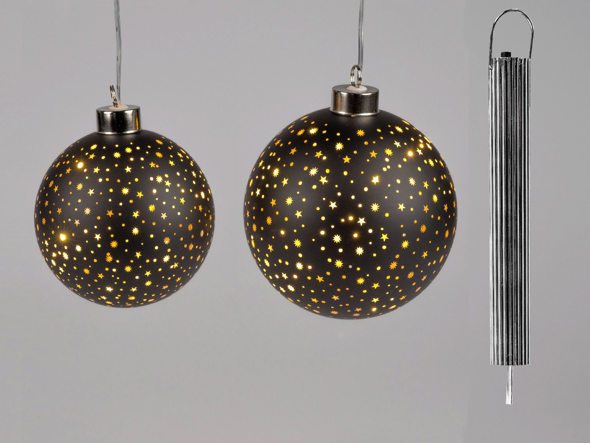 Zwei schwarze Weihnachtskugeln mit goldenen Sternen und ein silberner Kerzenhalter hängen vor einem