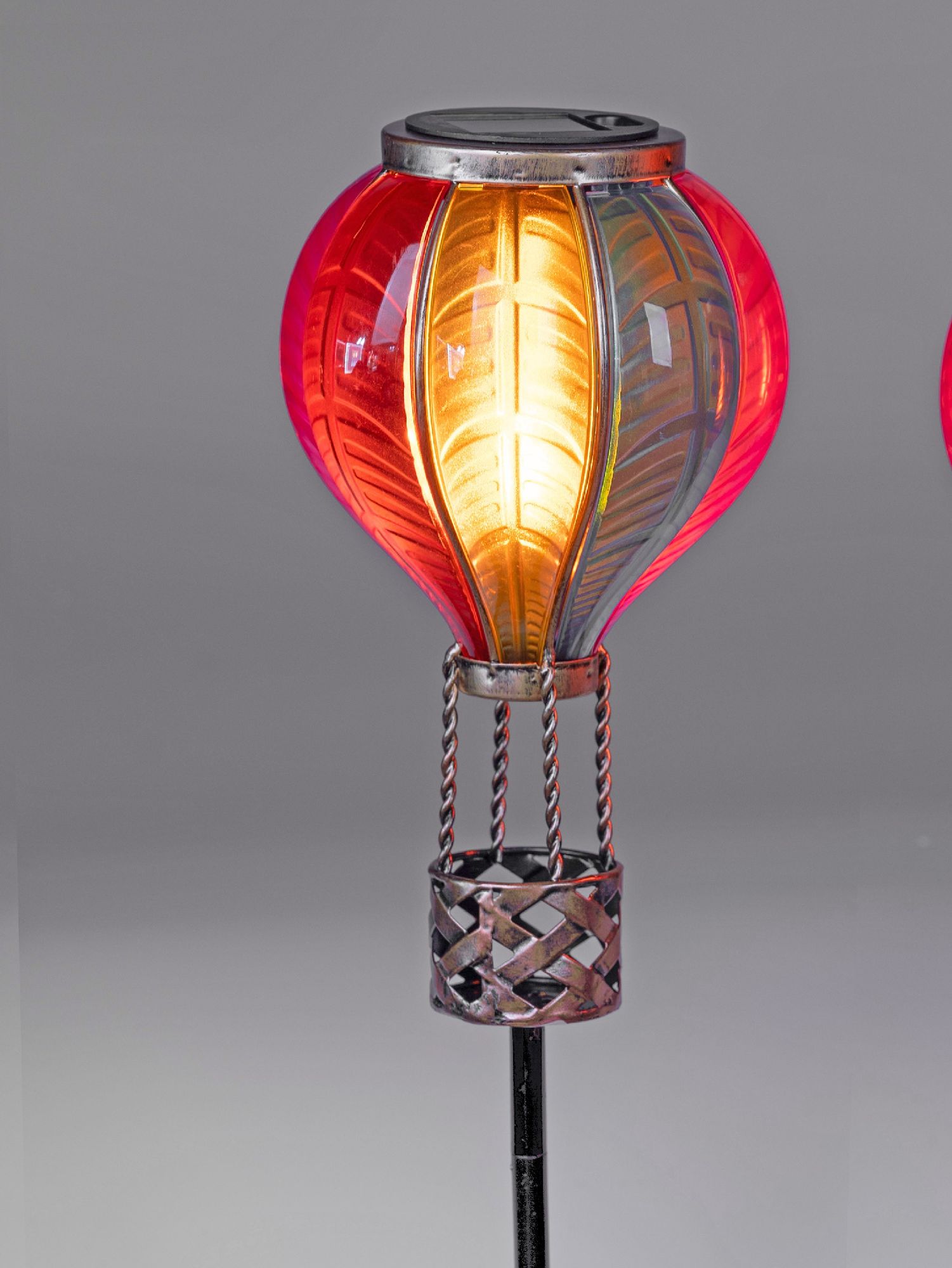 Bunte Laterne in Form eines Heißluftballons mit einem metallenen Korb, leuchtet in warmen Farben vor grauem Hintergrund.
