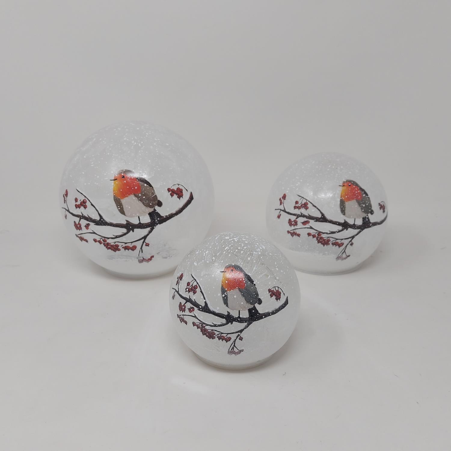Drei glitzernde Kugeln in Weiß mit Abbildungen von Vögeln auf einem Ast und roten Blättern.