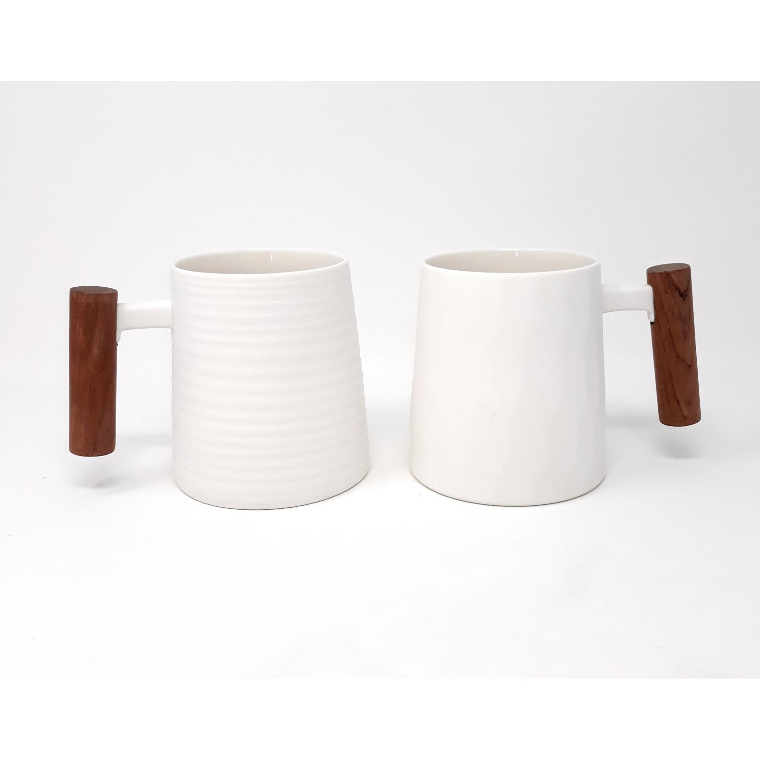 Zwei weiße Tassen mit Holzgriffen, eine mit gerippter Oberfläche, die andere glatt. Hintergrund ist neutral und hell.