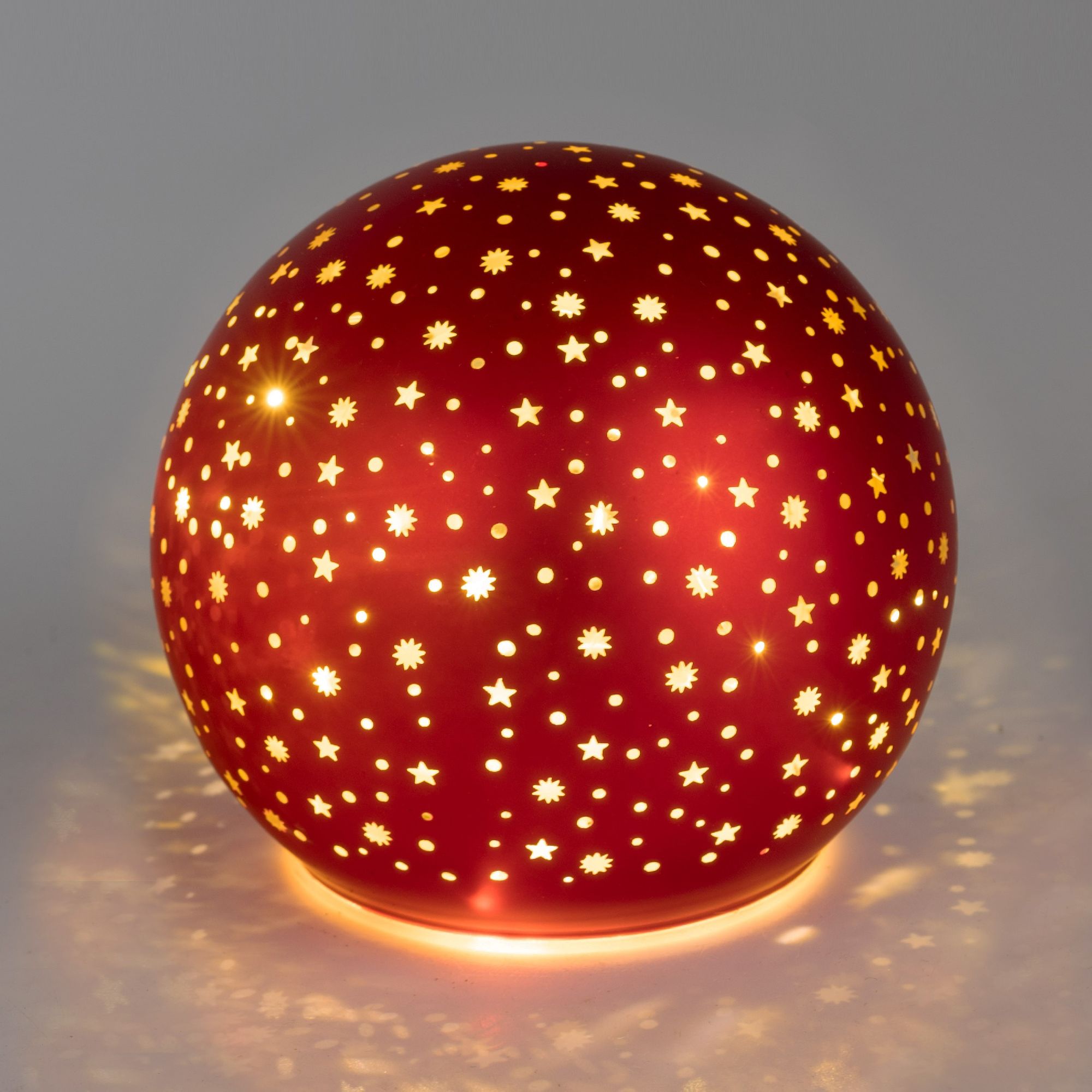 Runde, rote Lampe mit durchbrochenem Muster aus Sternen und Blumen, die warmes Licht abstrahlt und S