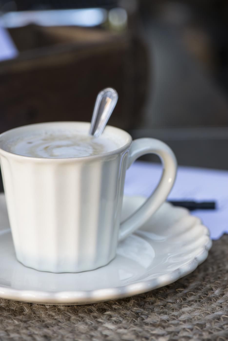 Eine weiße Tasse mit einem Löffel auf einem Unterteller, auf einem Tisch mit einer strukturierten Oberfläche.