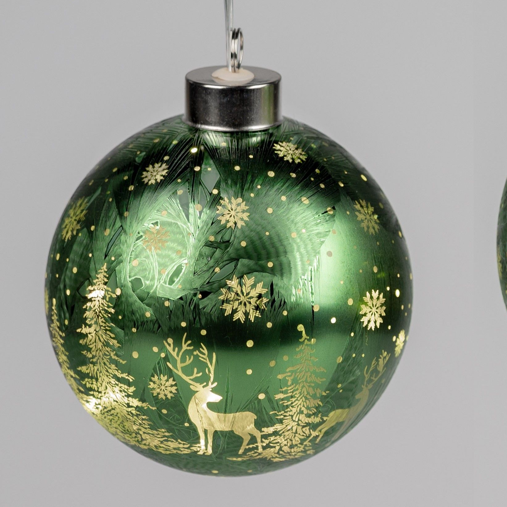 Grüne Weihnachtskugel mit goldenen Motiven von Rehen, Bäumen und Schneeflocken auf einer glatten Obe