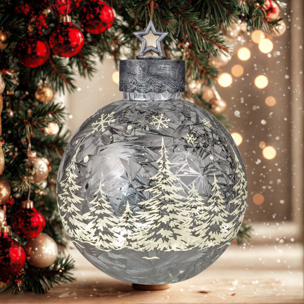 Leuchtende Dekokugel in silber mit weißen Tannenbäumen und Schneeflocken vor einem Weihnachtsbaum
