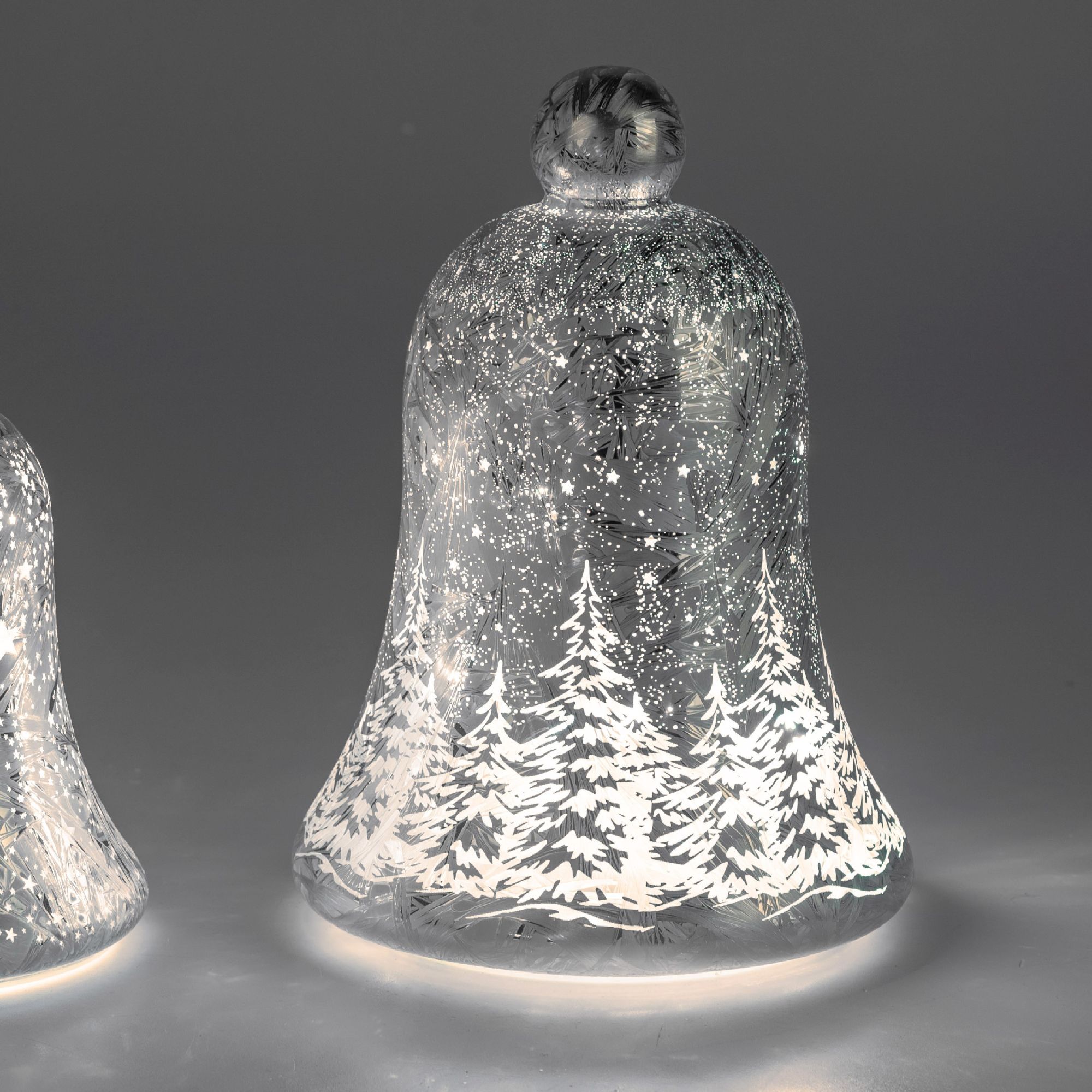 Zwei gläserne Glocken mit winterlichem Design, verziert mit weißen Tannenbäumen und glitzernden Schn