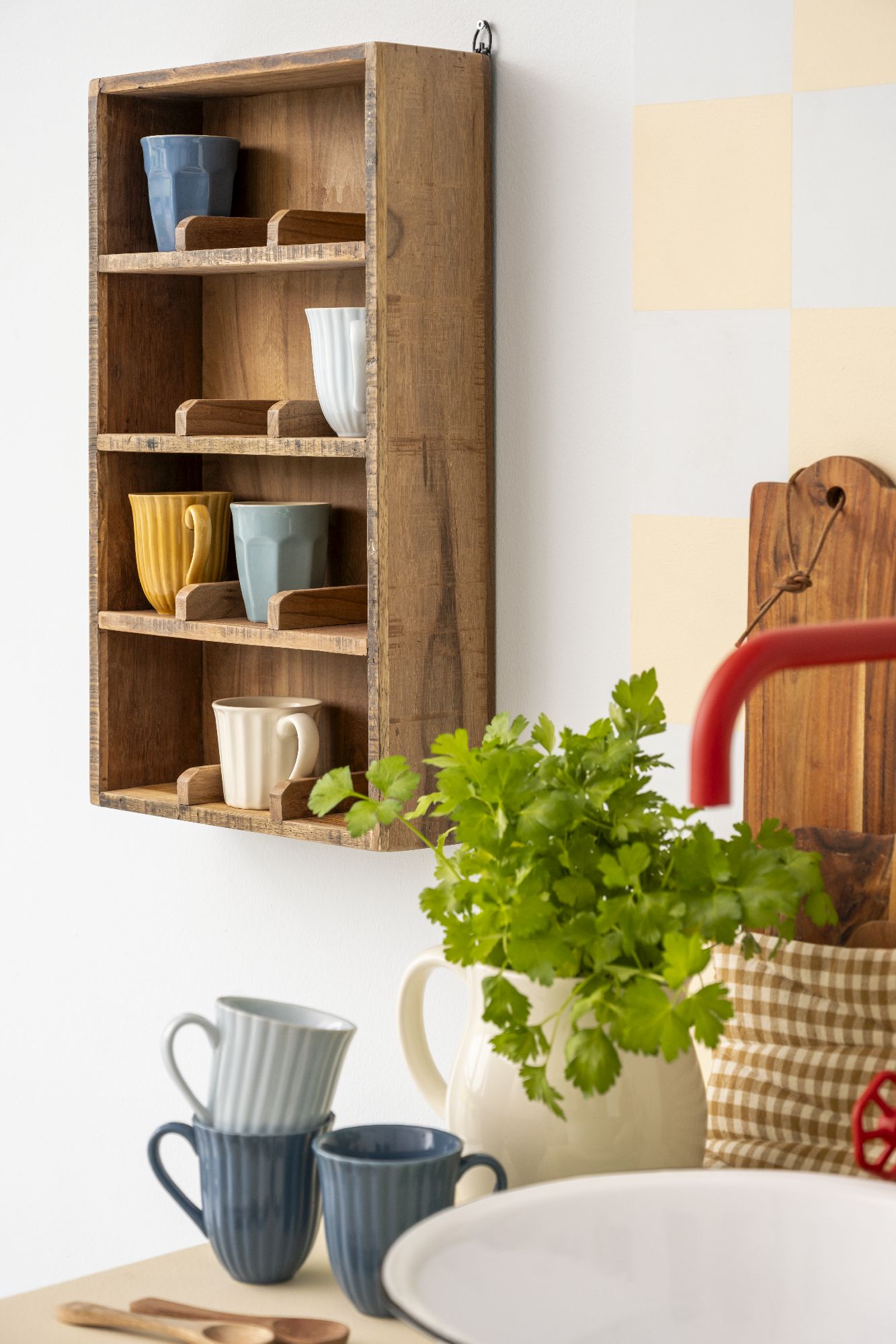 Ein Holzregal mit Tassen in verschiedenen Farben, darunter ein Topf mit frischer Petersilie und eine Schüssel.