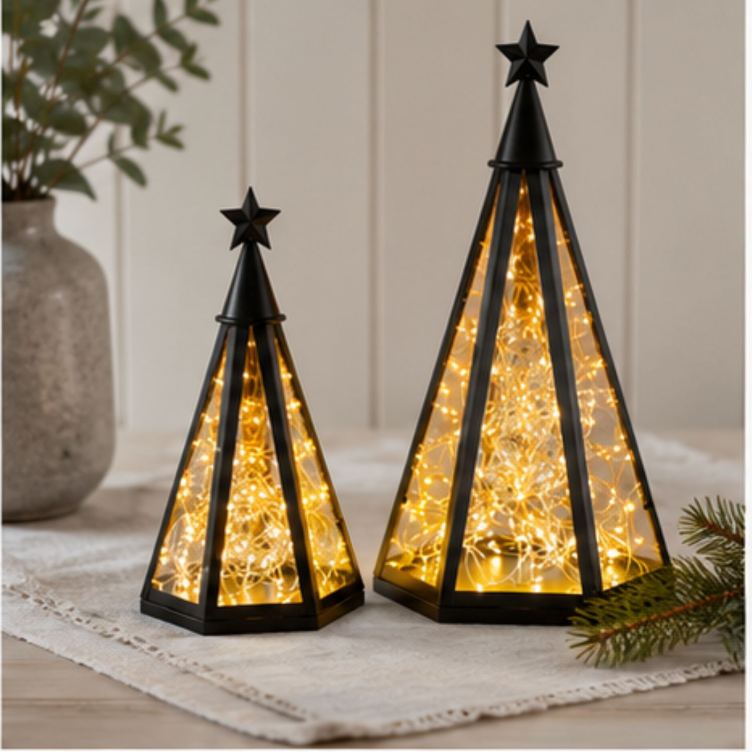 Zwei schwarze, pyramidenförmige Laternen mit warmen Lichterketten auf einem Tisch