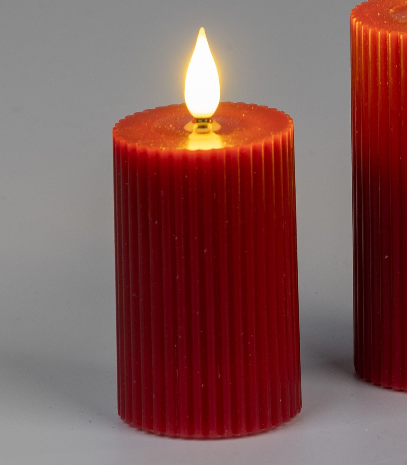 Zwei rote, gerippte Kerzen mit einer flackernden, künstlichen Flamme auf der Oberseite stehen vor ei