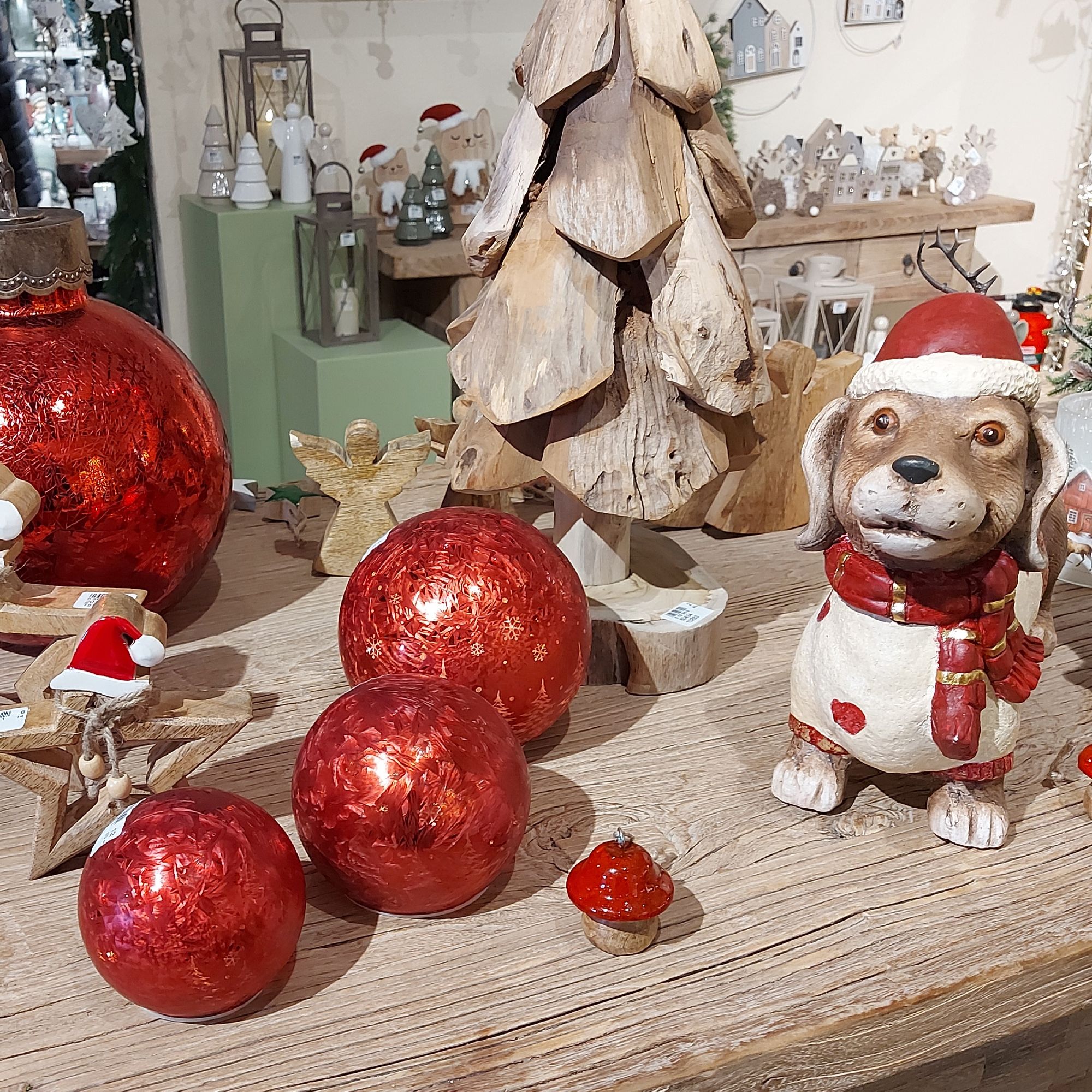 Dekorativer Tisch mit roten Weihnachtskugeln, einem Holzbaum, einem Hund aus Keramik und weiteren fe